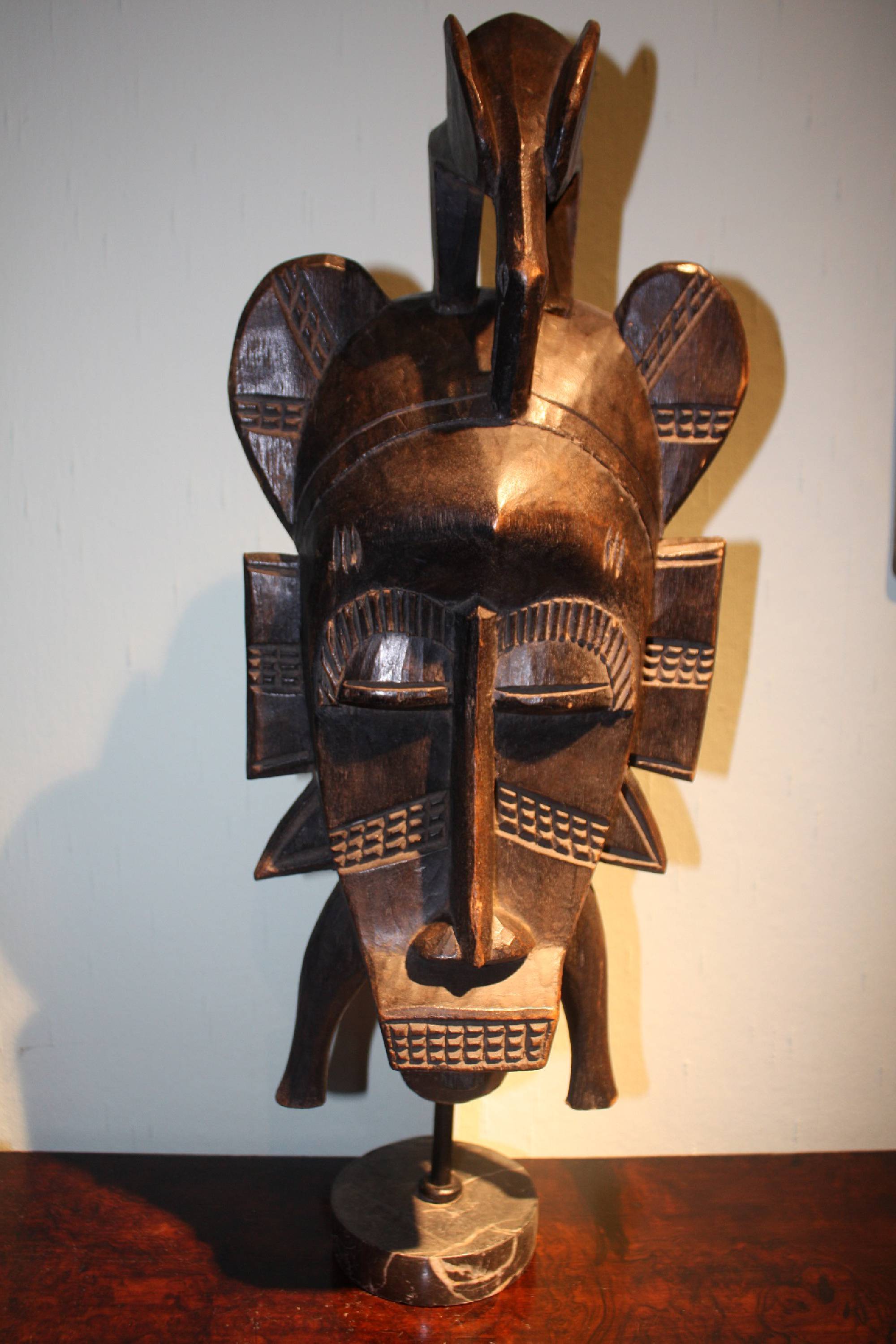 A large West-African handcarved wooden tribal Senufo ritual mask on a grey marble foot